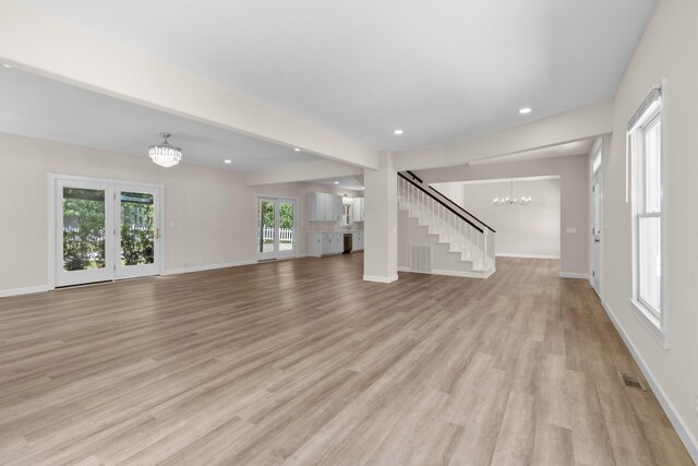 unfurnished living room featuring an inviting chandelier and light hardwood / wood-style floors