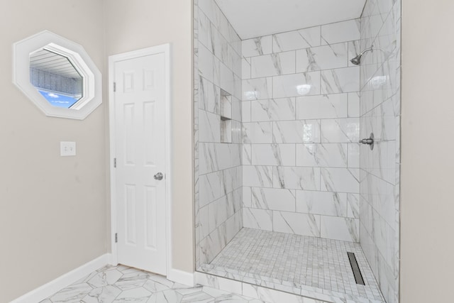 full bath featuring a tile shower, marble finish floor, and baseboards