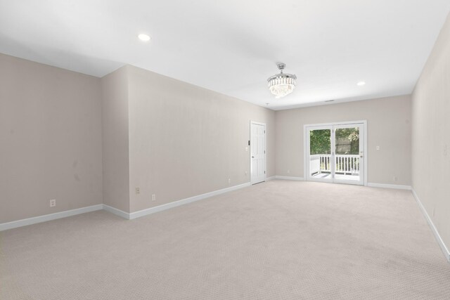 empty room with light colored carpet and an inviting chandelier