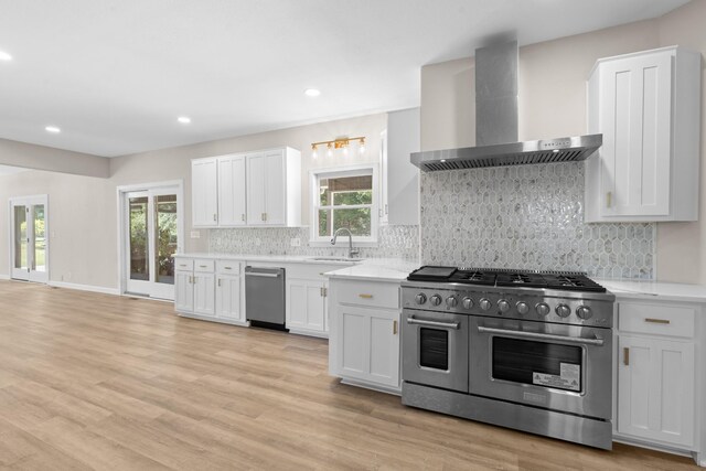 kitchen with stainless steel appliances, light hardwood / wood-style floors, white cabinetry, sink, and wall chimney exhaust hood