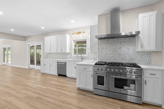 kitchen with wall chimney range hood, light wood-type flooring, decorative backsplash, appliances with stainless steel finishes, and a sink