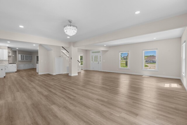 unfurnished living room with light wood-type flooring and an inviting chandelier