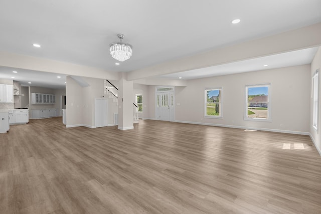 unfurnished living room featuring light wood-type flooring, baseboards, an inviting chandelier, and stairs