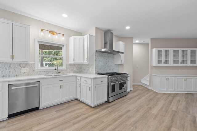 kitchen featuring wall chimney range hood, white cabinets, stainless steel appliances, and sink