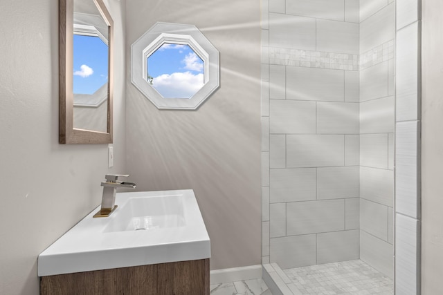 bathroom featuring a tile shower, marble finish floor, vanity, and baseboards