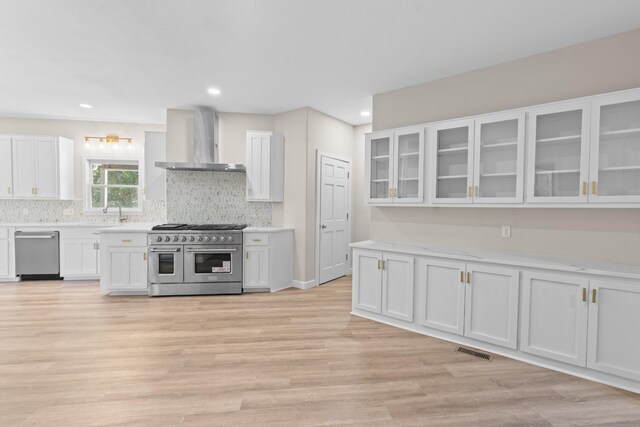 kitchen with backsplash, light hardwood / wood-style floors, stainless steel appliances, white cabinetry, and wall chimney range hood