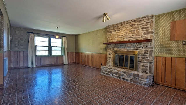 unfurnished living room featuring a wainscoted wall, brick patterned floor, a fireplace, and wallpapered walls