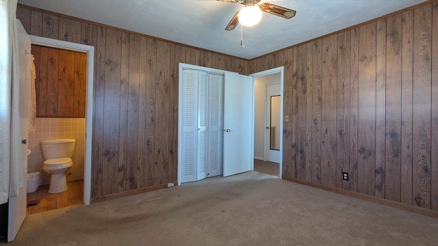 unfurnished bedroom with wood walls, ornamental molding, a closet, and light colored carpet