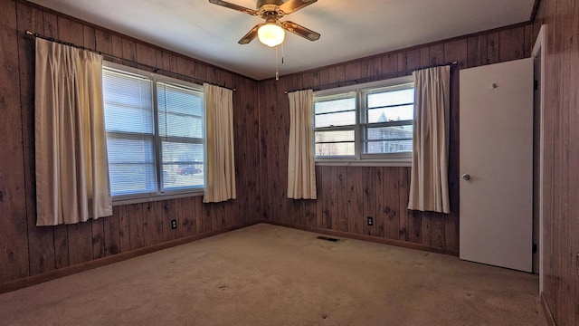 empty room with a healthy amount of sunlight, wood walls, ceiling fan, and visible vents