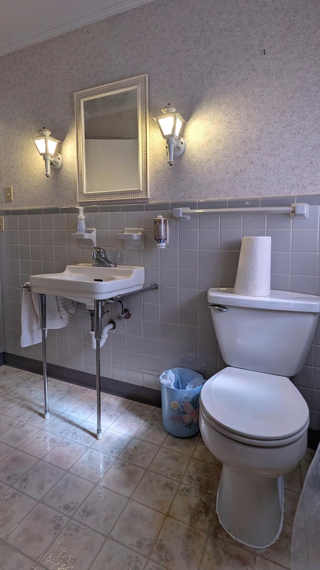 bathroom featuring wallpapered walls, wainscoting, toilet, tile patterned flooring, and crown molding