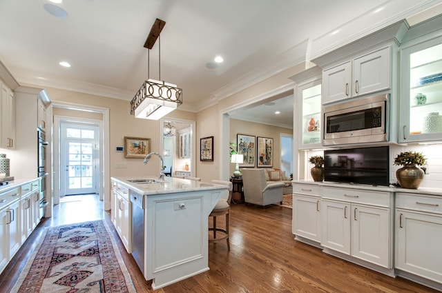 kitchen with white cabinets, stainless steel appliances, sink, dark hardwood / wood-style floors, and a center island with sink