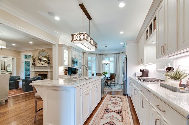 kitchen with white cabinets, hanging light fixtures, light hardwood / wood-style flooring, sink, and a center island with sink