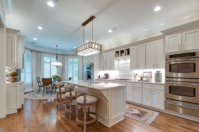 kitchen with a kitchen island with sink, hardwood / wood-style floors, crown molding, stainless steel appliances, and decorative light fixtures