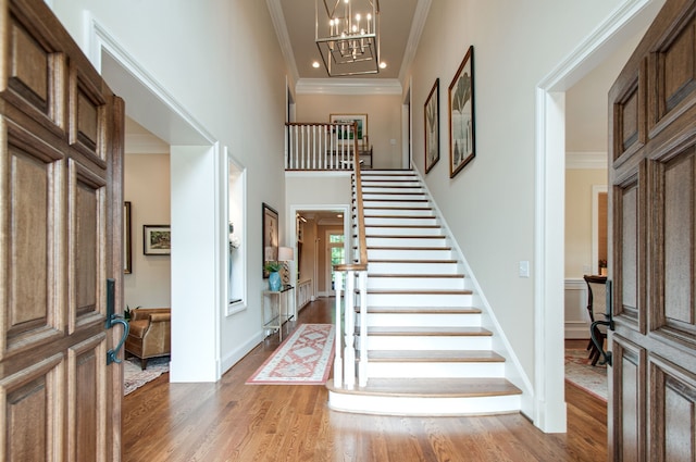 foyer with wood-type flooring, a chandelier, crown molding, and a towering ceiling