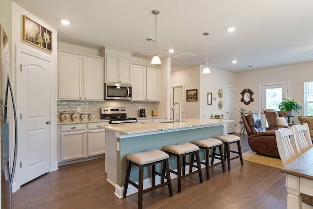 kitchen with decorative light fixtures, stainless steel appliances, dark hardwood / wood-style flooring, sink, and a center island with sink