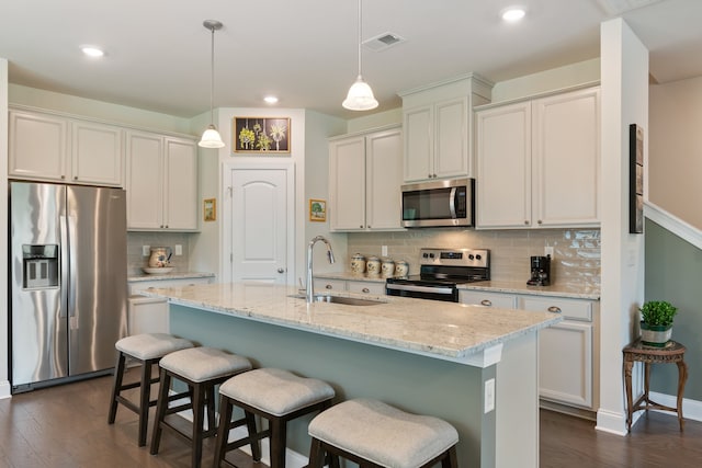 kitchen with dark hardwood / wood-style floors, light stone countertops, a kitchen island with sink, hanging light fixtures, and stainless steel appliances