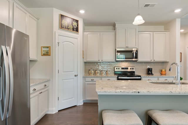 kitchen with white cabinetry, stainless steel appliances, light stone countertops, hanging light fixtures, and dark wood-type flooring