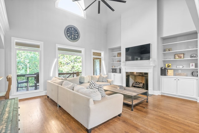 living room with light wood-type flooring, built in shelves, a towering ceiling, and a tile fireplace