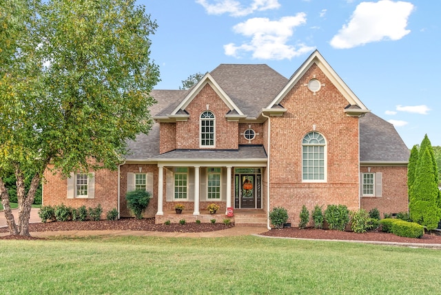 traditional-style house with brick siding, roof with shingles, and a front lawn