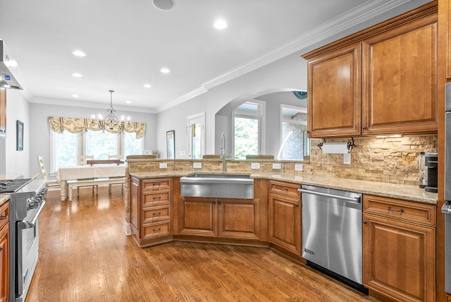 kitchen with light stone countertops, decorative backsplash, brown cabinets, stainless steel appliances, and a sink