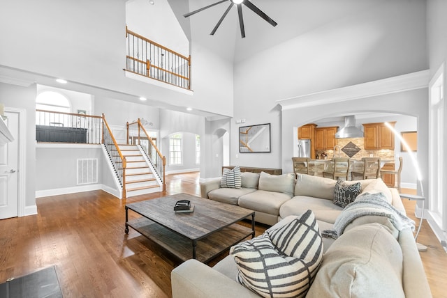 living room featuring visible vents, baseboards, stairway, wood finished floors, and arched walkways