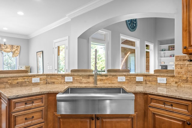 kitchen featuring ornamental molding, light stone counters, built in features, arched walkways, and brown cabinetry