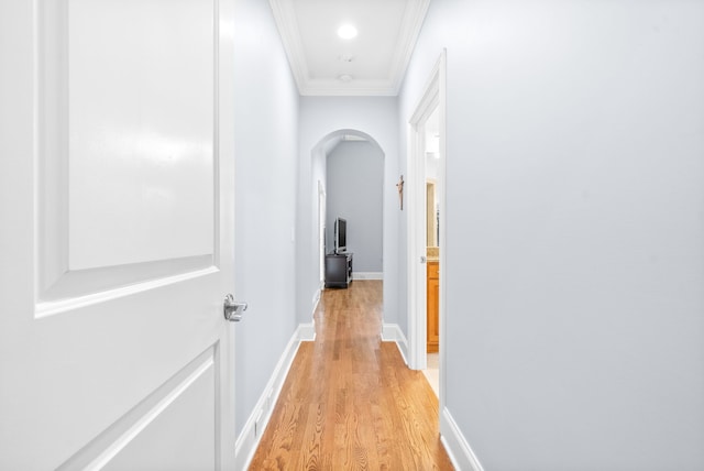 hall featuring crown molding, baseboards, arched walkways, and light wood-type flooring