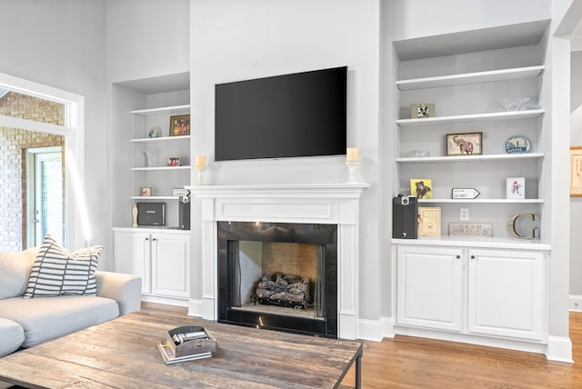 living room featuring built in shelves, a fireplace, light wood-type flooring, and baseboards