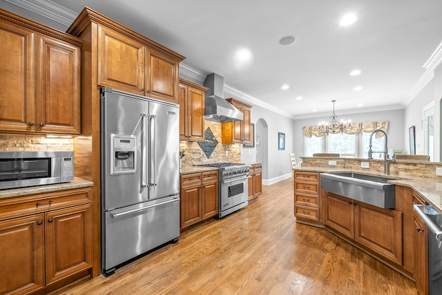 kitchen featuring brown cabinets, high quality appliances, a sink, arched walkways, and wall chimney range hood