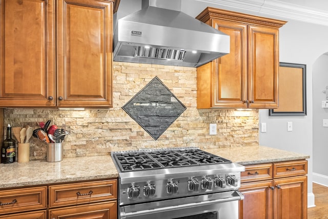 kitchen with tasteful backsplash, high end range, brown cabinets, and wall chimney exhaust hood