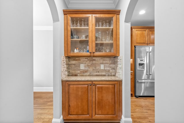 bar with backsplash, ornamental molding, high end refrigerator, and light wood finished floors