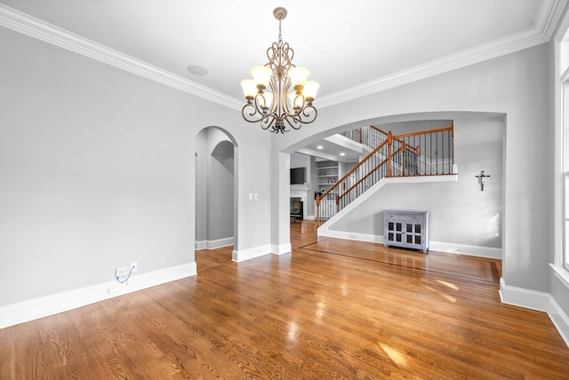 unfurnished living room featuring wood finished floors, an inviting chandelier, a fireplace, stairs, and crown molding