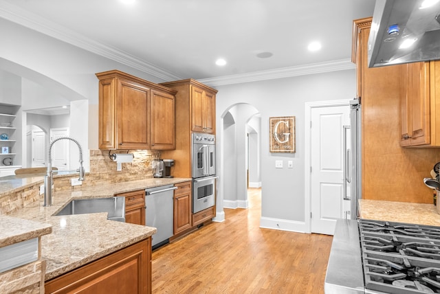 kitchen featuring light stone counters, brown cabinets, appliances with stainless steel finishes, arched walkways, and a sink