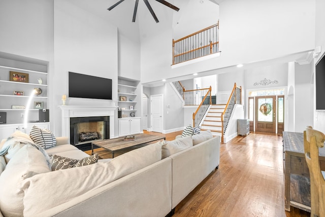 living room featuring built in shelves, wood finished floors, baseboards, a fireplace, and stairs