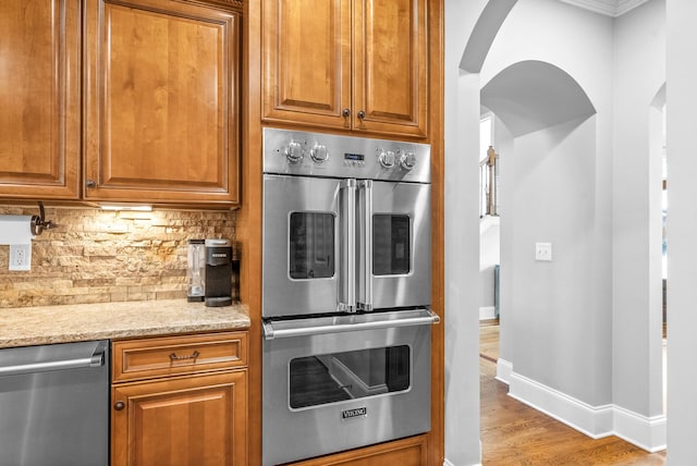 kitchen with arched walkways, backsplash, appliances with stainless steel finishes, and brown cabinets