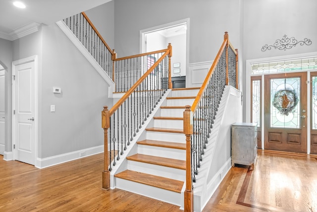 foyer entrance with wood finished floors, baseboards, recessed lighting, ornamental molding, and a towering ceiling