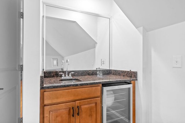 kitchen featuring beverage cooler, lofted ceiling, dark stone countertops, brown cabinetry, and a sink