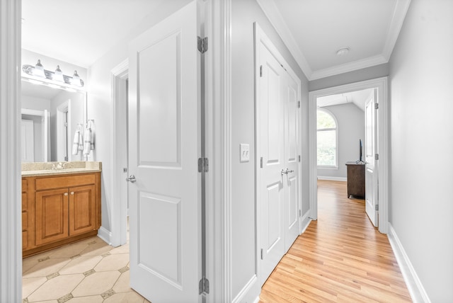 hall featuring crown molding, light wood-style flooring, and baseboards