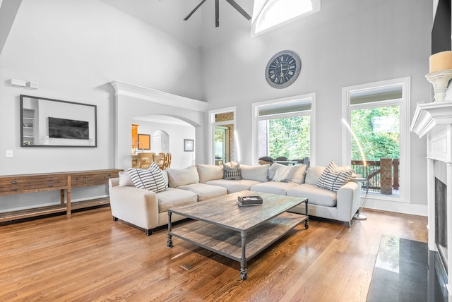 living room with a high ceiling, light wood-type flooring, arched walkways, and a premium fireplace