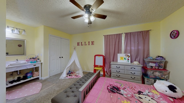 carpeted bedroom with a textured ceiling, ceiling fan, sink, and a closet