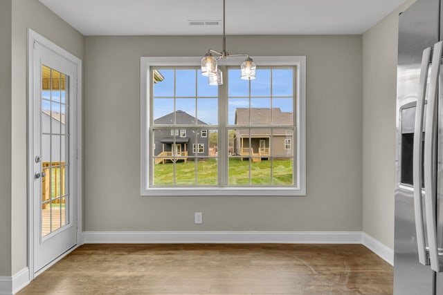 unfurnished dining area featuring a wealth of natural light, hardwood / wood-style floors, and a notable chandelier