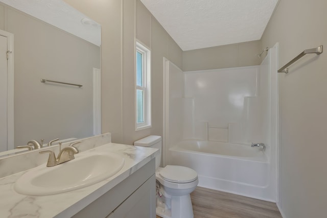 full bathroom featuring hardwood / wood-style floors, toilet, vanity, washtub / shower combination, and a textured ceiling