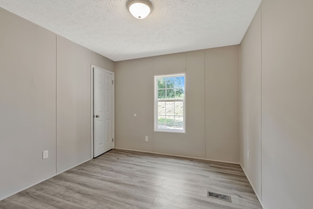 empty room with a textured ceiling and light hardwood / wood-style flooring