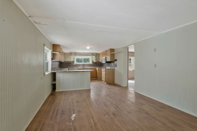 kitchen with light brown cabinetry, tasteful backsplash, light hardwood / wood-style floors, crown molding, and kitchen peninsula