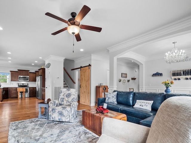 living room with ceiling fan, ornamental molding, a barn door, and light hardwood / wood-style floors