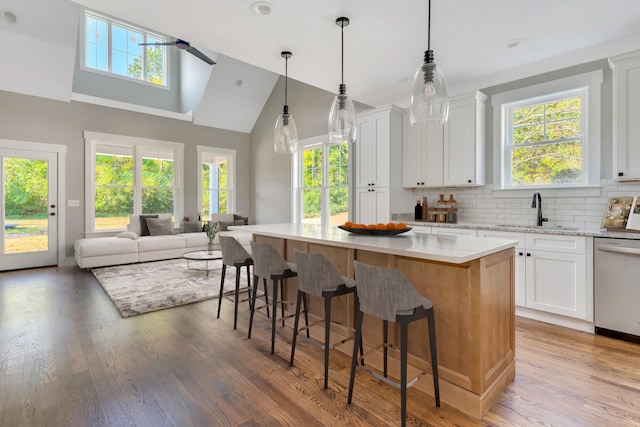 kitchen featuring hardwood / wood-style floors, stainless steel dishwasher, a kitchen island, and white cabinets