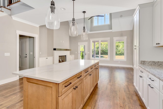 kitchen featuring a kitchen island, hanging light fixtures, white cabinetry, light stone counters, and light hardwood / wood-style flooring