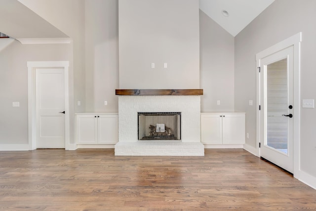 unfurnished living room featuring high vaulted ceiling, light wood-type flooring, and a brick fireplace