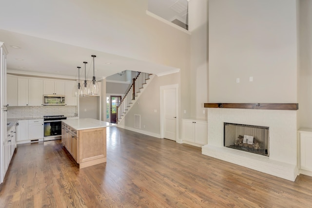 kitchen with a kitchen island, hanging light fixtures, white cabinetry, stainless steel appliances, and hardwood / wood-style flooring