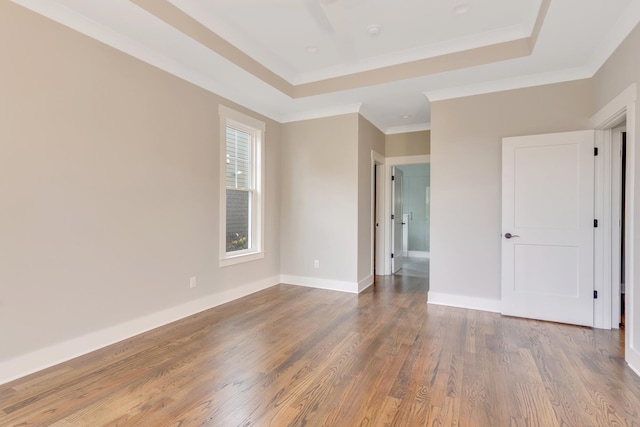 empty room featuring crown molding, wood-type flooring, and a tray ceiling